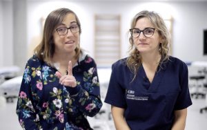Alicia Martínez, paciente de Alcer Castalia, y la profesora del Grado en Fisioterapia de la CEU UCH, Eva Segura, explican a los pacientes en hemodiálisis las ventajas de realizar ejercicio en uno de los vídeos.